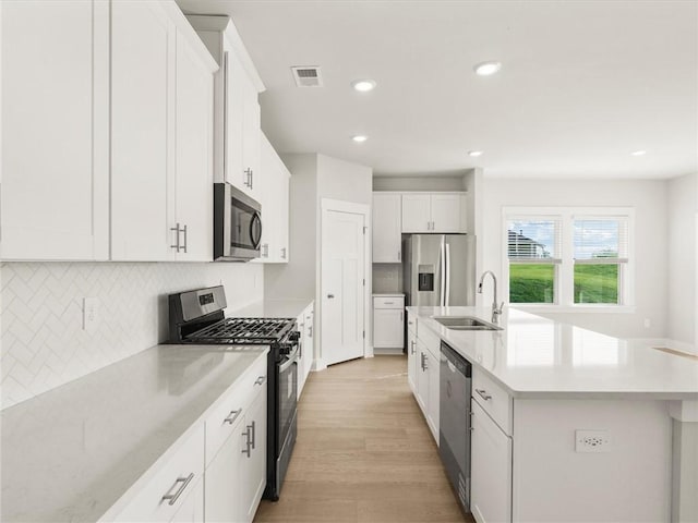 kitchen featuring stainless steel appliances, a sink, an island with sink, white cabinets, and backsplash