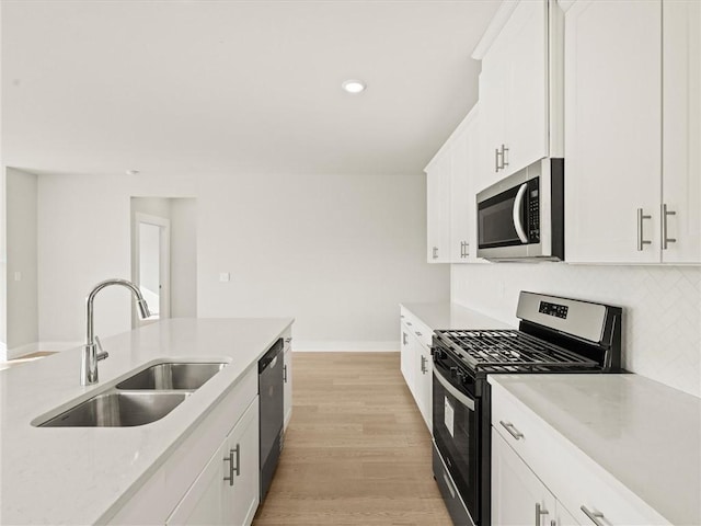 kitchen featuring stainless steel appliances, a sink, light wood-type flooring, white cabinets, and baseboards