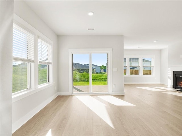 unfurnished living room with healthy amount of natural light, light wood-type flooring, a lit fireplace, and recessed lighting
