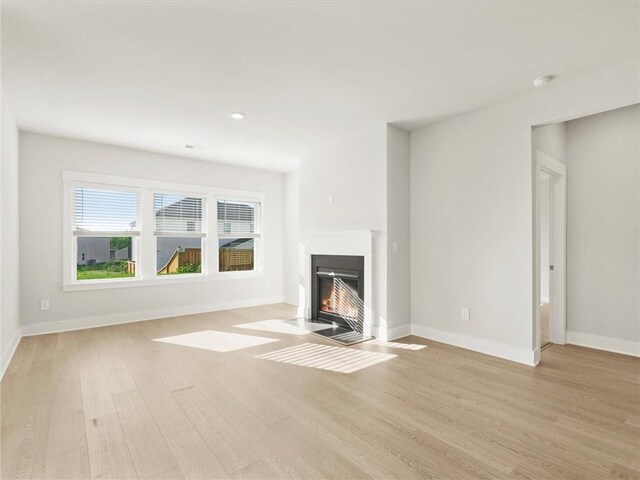 unfurnished living room featuring light wood-style flooring, a fireplace with flush hearth, and baseboards