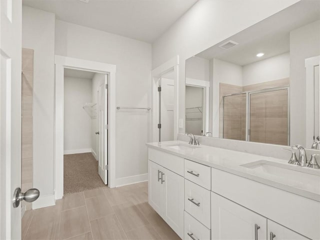 bathroom with a walk in closet, double vanity, a shower stall, and baseboards