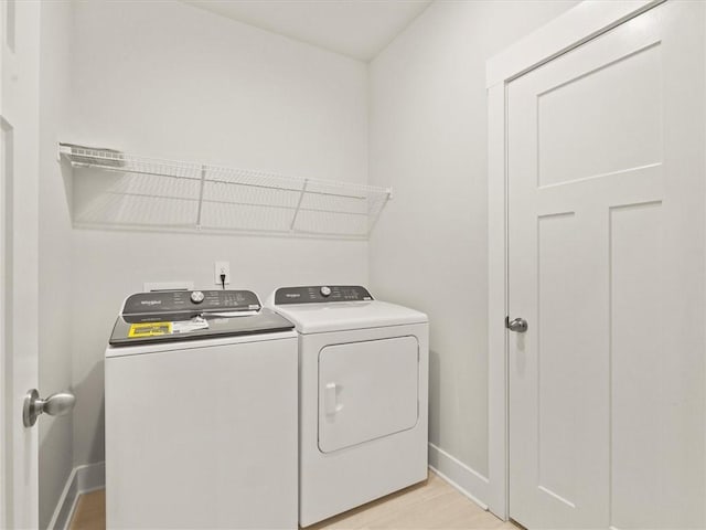 washroom featuring washing machine and dryer, baseboards, and light wood-style flooring