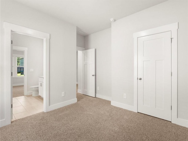 unfurnished bedroom with light colored carpet, ensuite bath, and baseboards