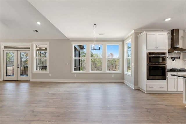 kitchen featuring a notable chandelier, white cabinetry, visible vents, wall chimney exhaust hood, and light wood finished floors