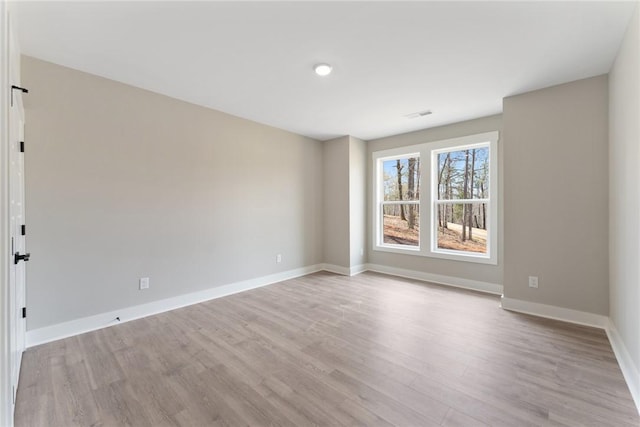 empty room with light wood finished floors, baseboards, and visible vents