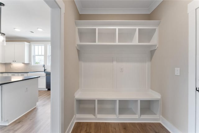 mudroom with crown molding, baseboards, light wood-style floors, and a sink