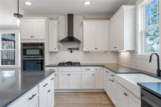 kitchen with white cabinets, wall chimney exhaust hood, a sink, dark countertops, and appliances with stainless steel finishes