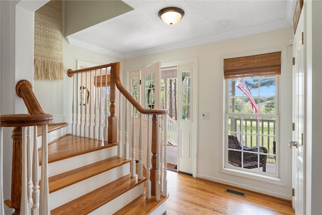 stairway featuring ornamental molding, visible vents, wood finished floors, and a textured ceiling
