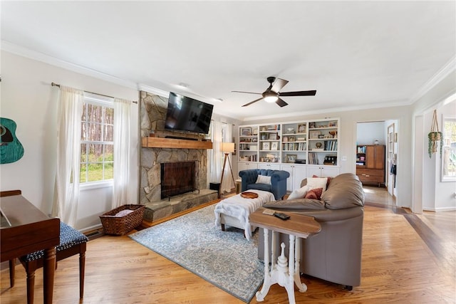 living room with light wood-type flooring, ceiling fan, crown molding, and a stone fireplace