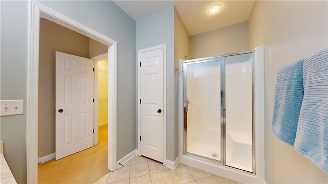 bathroom featuring tile patterned flooring, baseboards, a walk in closet, and a stall shower