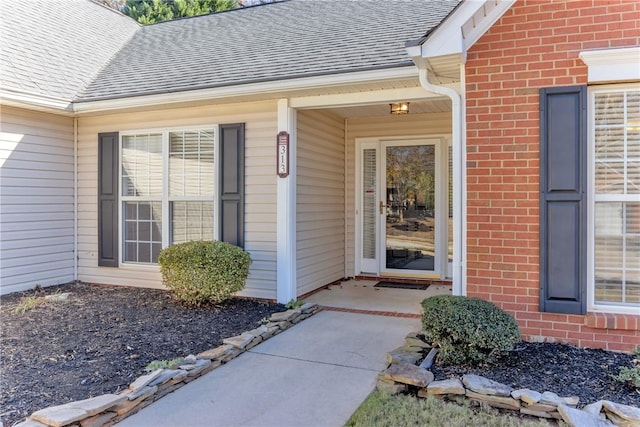 view of exterior entry with brick siding and roof with shingles