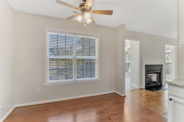 unfurnished living room with ceiling fan, light wood-type flooring, baseboards, and a healthy amount of sunlight
