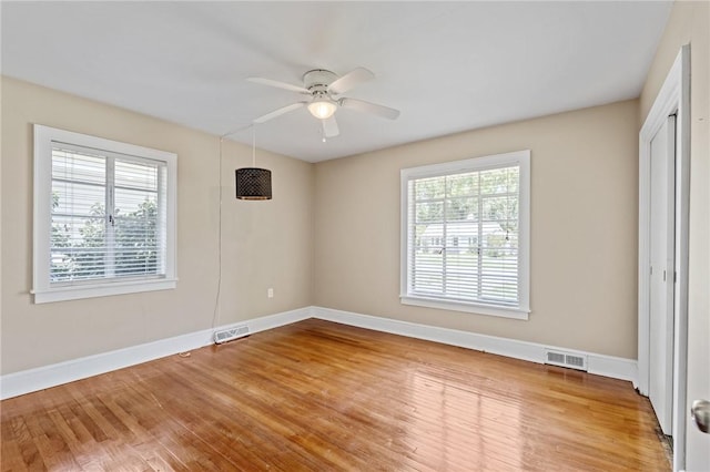 unfurnished room with wood finished floors, baseboards, a ceiling fan, and visible vents