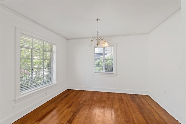 spare room featuring ornamental molding, baseboards, hardwood / wood-style floors, and a notable chandelier