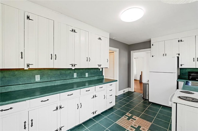 kitchen with tasteful backsplash, dark tile patterned flooring, white cabinetry, and white appliances