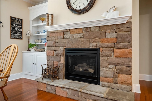 interior details with built in features, baseboards, a stone fireplace, crown molding, and wood finished floors