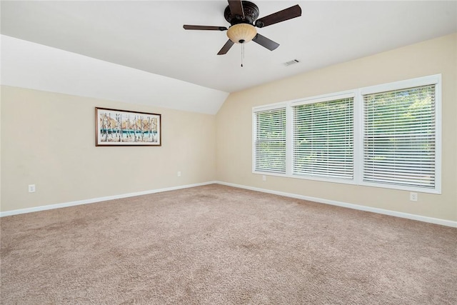 carpeted spare room featuring a ceiling fan, baseboards, vaulted ceiling, and visible vents