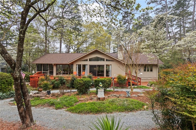 back of house featuring a shingled roof, a sunroom, and a chimney
