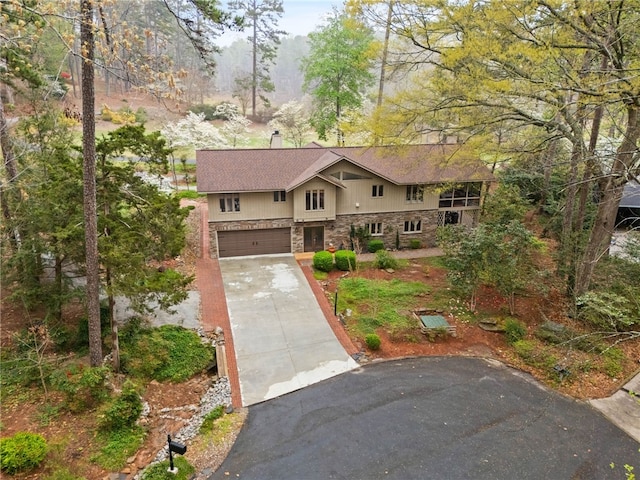 view of front facade with concrete driveway, stone siding, a garage, and a chimney