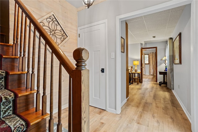 foyer entrance featuring light wood-style floors, a paneled ceiling, stairs, and baseboards