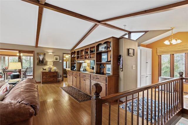 living area featuring lofted ceiling with beams, a wealth of natural light, light wood-style floors, and a notable chandelier