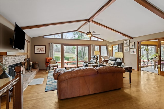 living area with vaulted ceiling with beams, a brick fireplace, a ceiling fan, and light wood-style flooring