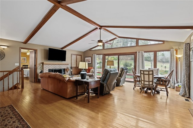living room with light wood-style flooring, a ceiling fan, vaulted ceiling with beams, and a brick fireplace