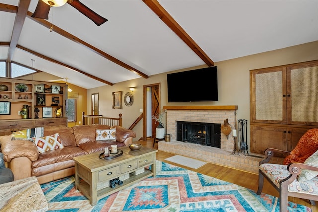 living area with ceiling fan, wood finished floors, a fireplace, and lofted ceiling with beams