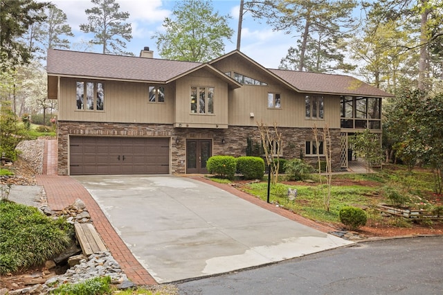 view of front facade with roof with shingles, a chimney, driveway, stone siding, and a garage
