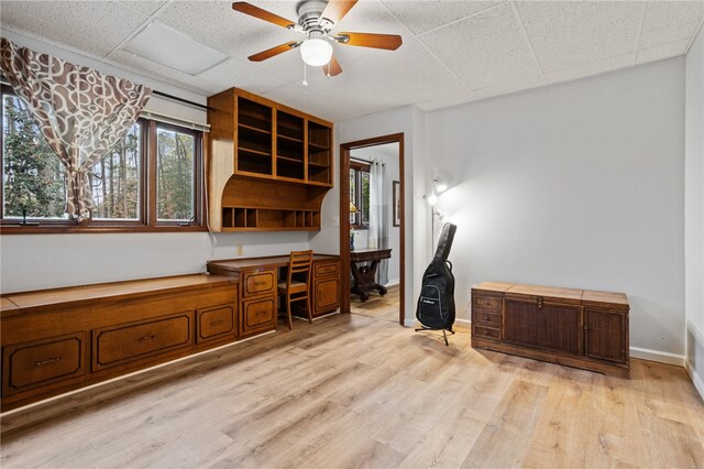 unfurnished office featuring built in desk, light wood-type flooring, a healthy amount of sunlight, and a ceiling fan