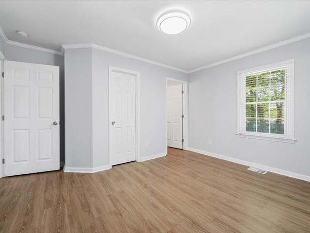 unfurnished bedroom with wood finished floors, visible vents, ornamental molding, and baseboards