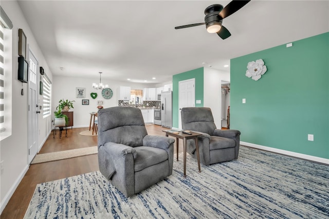 living room with ceiling fan with notable chandelier, baseboards, and wood finished floors