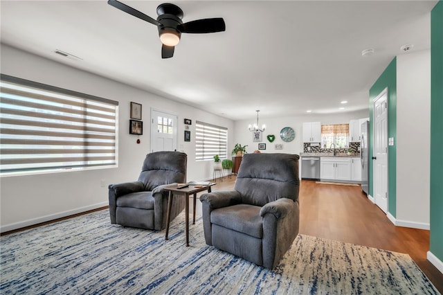 living area with light wood-style flooring, ceiling fan with notable chandelier, baseboards, and a wealth of natural light