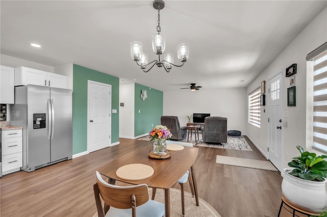 dining area with light wood-style floors, ceiling fan with notable chandelier, and baseboards