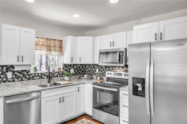 kitchen with appliances with stainless steel finishes, decorative backsplash, a sink, and white cabinets