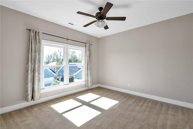 carpeted spare room with baseboards, a ceiling fan, and visible vents