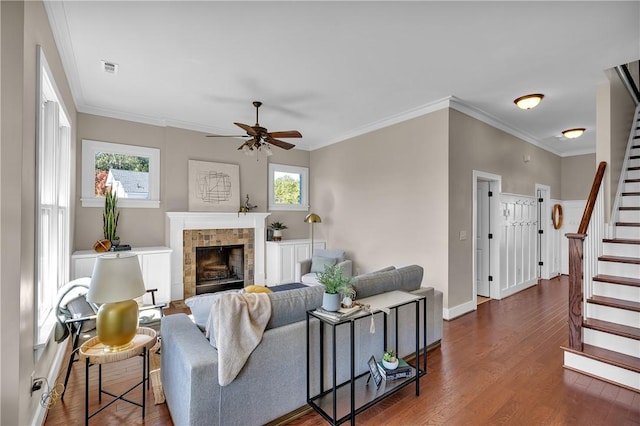 living area with stairway, a ceiling fan, baseboards, dark wood-style flooring, and a brick fireplace