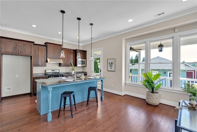 kitchen with an island with sink, under cabinet range hood, visible vents, appliances with stainless steel finishes, and a breakfast bar area