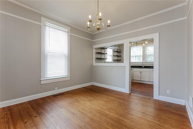 unfurnished dining area featuring visible vents, baseboards, a chandelier, crown molding, and hardwood / wood-style floors