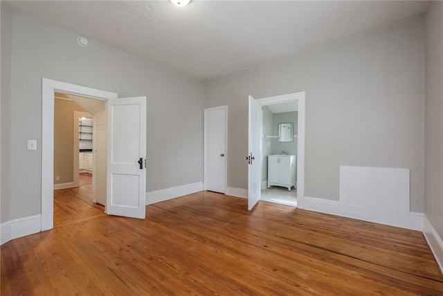 unfurnished bedroom featuring light wood finished floors, baseboards, ensuite bathroom, and vaulted ceiling
