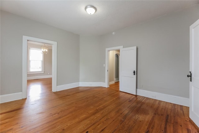 unfurnished room with a chandelier, light wood-style flooring, and baseboards