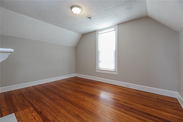 bonus room featuring a textured ceiling, vaulted ceiling, visible vents, wood finished floors, and baseboards