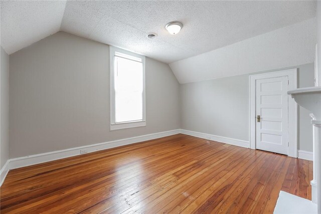 additional living space with light wood-style floors, a textured ceiling, baseboards, and lofted ceiling