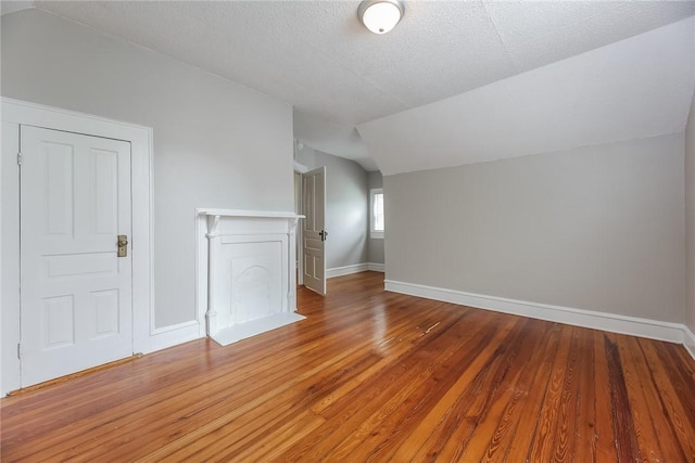 additional living space featuring light wood-style floors, baseboards, vaulted ceiling, and a textured ceiling
