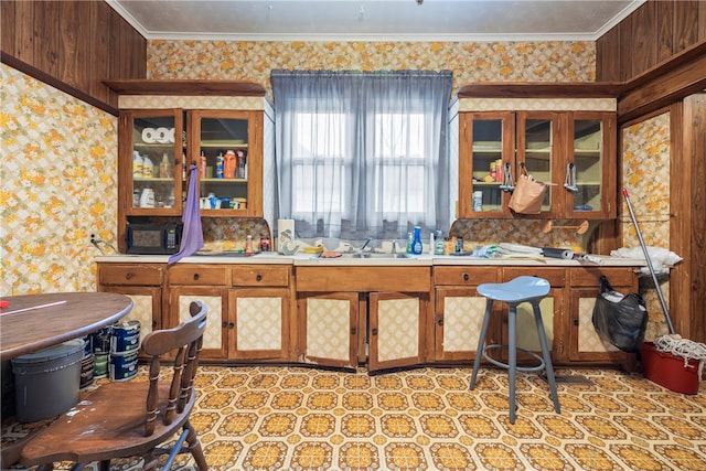kitchen featuring glass insert cabinets, wallpapered walls, crown molding, and light floors