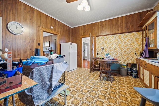 kitchen featuring ornamental molding, wooden walls, a ceiling fan, freestanding refrigerator, and brown cabinetry