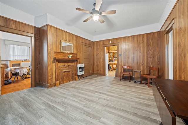 interior space featuring ornamental molding, a ceiling fan, heating unit, light wood-style floors, and wooden walls