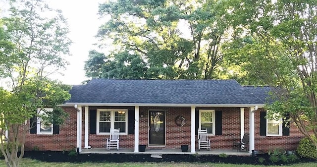 single story home featuring roof with shingles, brick siding, and covered porch