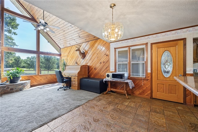 foyer featuring wood walls, stone finish floor, plenty of natural light, and ceiling fan with notable chandelier