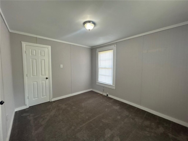 spare room with baseboards, ornamental molding, and dark colored carpet